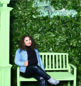 Ashlea on a green bench in front of a sign that says 'trust the journey'