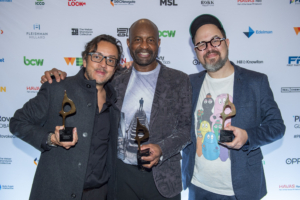 Three men hold statues won by The Weber Shandwick Collective at the 2023 Global SABRE Awards
