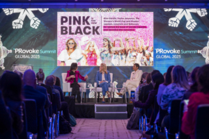 Weber Shandwick CEO Gail Heimann, Journalist and Author Candace Bushnell and Powell Tate Senior Advisor and CBS News Senior Political Contributor Ashley Etienne are onstage for a panel discussion titled "Pink is the New Black" at the 2023 PRovoke Global Summit in Washington, DC. They are seated in padded chairs in front of a screen displaying a presentation which features a number of prominent female entertainers, politicians and figures from the Summer of 2023.