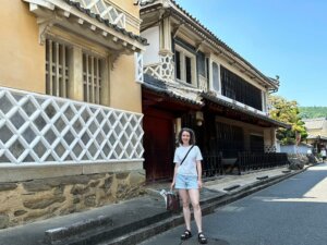 Image of a woman standing in front of a building in Japan wearing shorts and a crossbody bag.